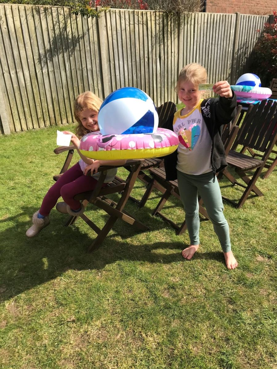 Two little girls displaying their land train tickets, and they have constructed two deck chairs into the form of a train in their garden