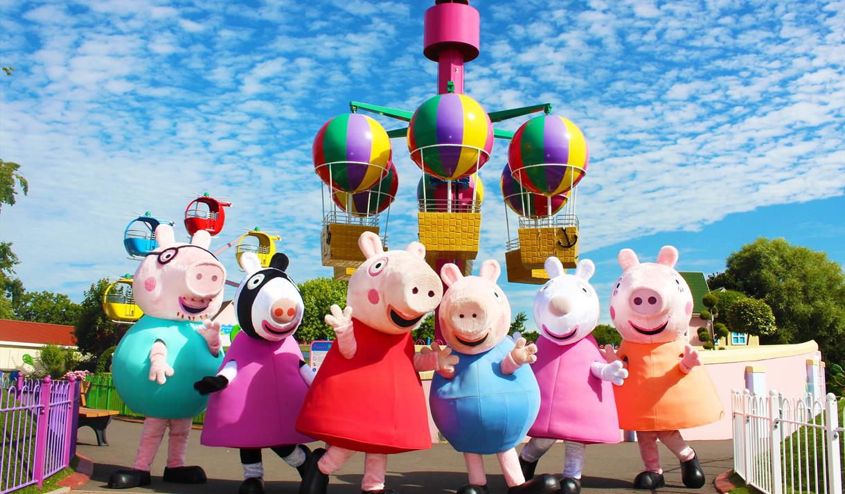 Peppa Pig and her family standing outside with roller-coaster in the background