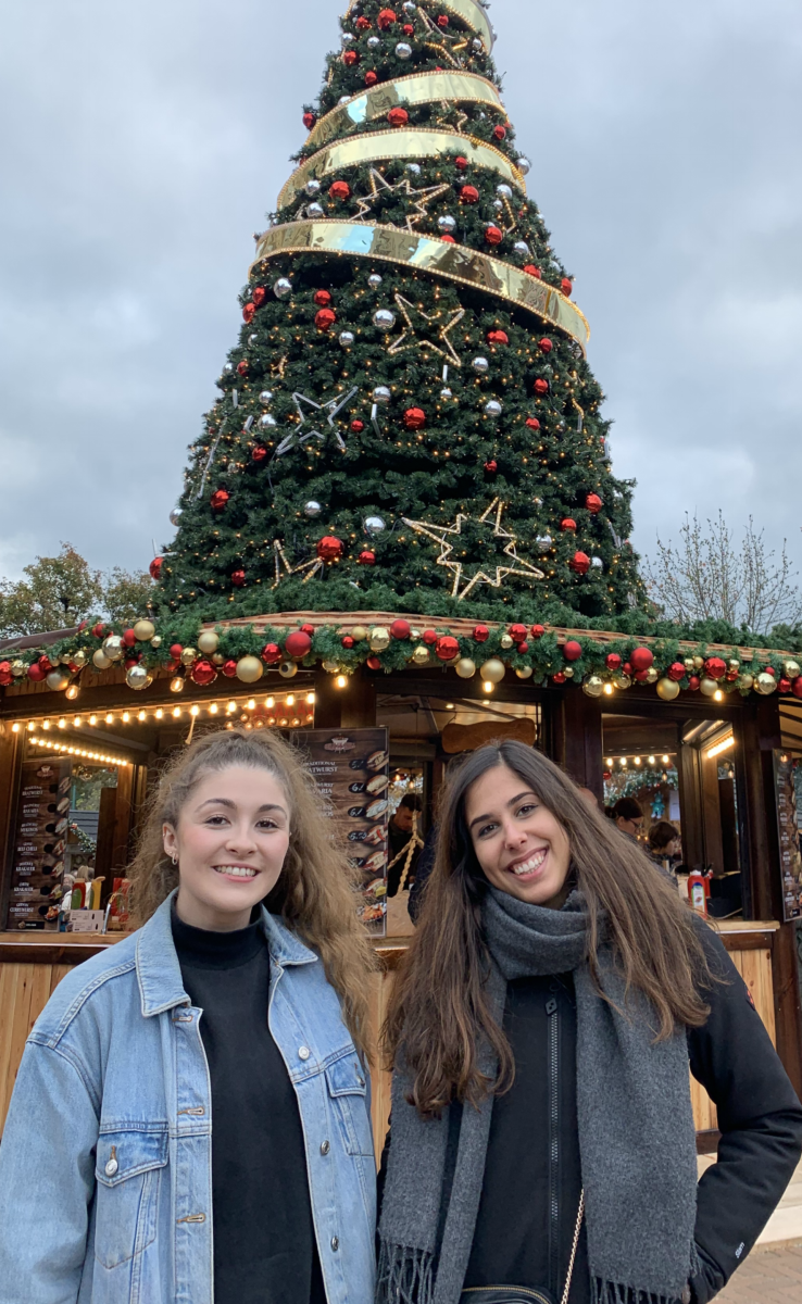 Two ladies standing in front of a tree in the Bournemouth Alpine market at this years Christmas Tree Wonderland.