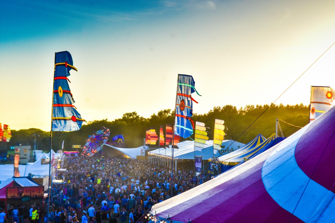 An elevated view of a packed crowd between rows of tents as the sun sets on the Bournemouth 7s festival.