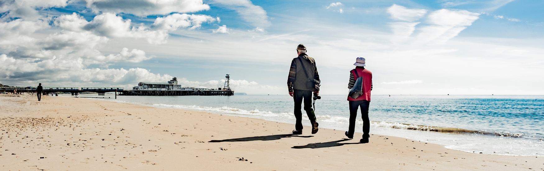 Couple enjoying a winter walk along Bournemouth beach as they head towards the pier 