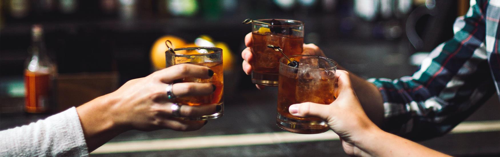 Three arms cheering their drinks together in a bar