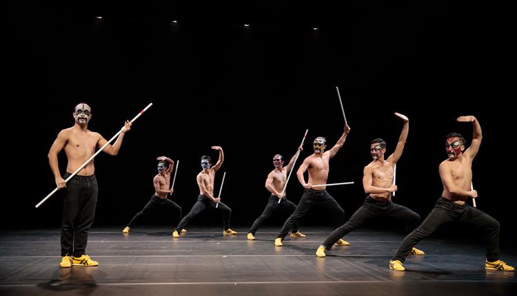 Seven dancers on stage striking a pose with poles