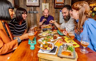 Five people around a table enjoying a selection of food and beer.
