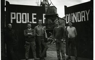 A black and white image with 5 men stood in front of Poole Foundry gates