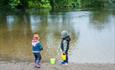 Two children playing in the river with buckets