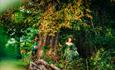 Models dressed up in green with vines and pinecones on them in the woods