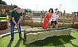 Family watching dad try to hit golf ball through rocky obstacle into the hole