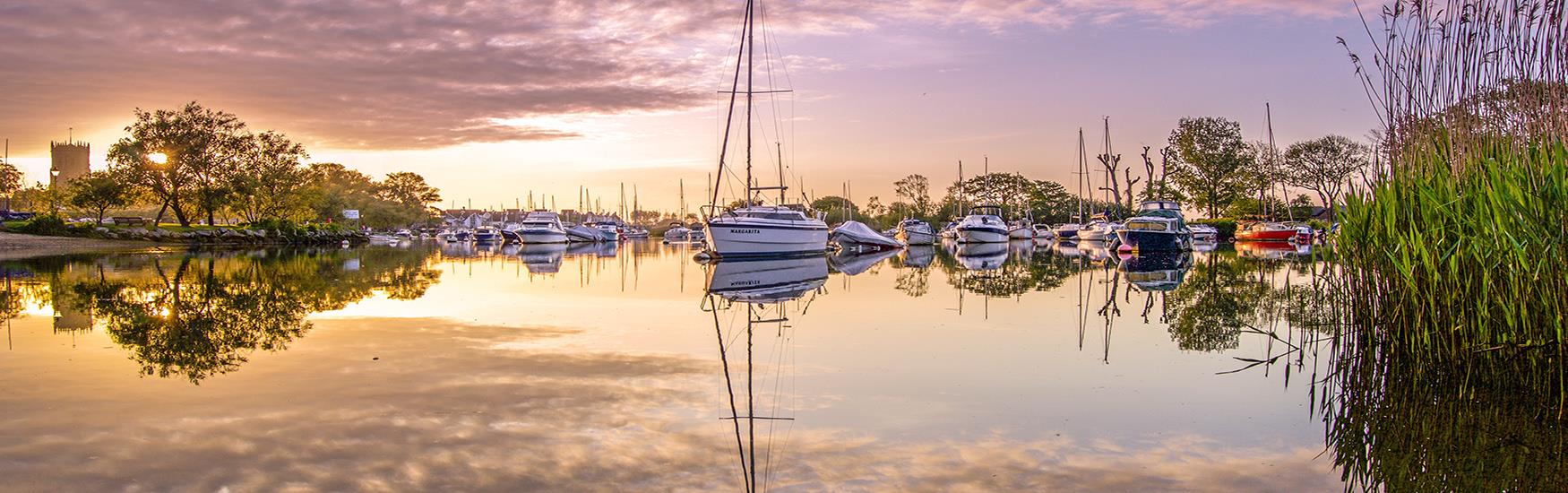 Stunning sunset over Christchurch harbour with boats moored and reflecting of the glassy water