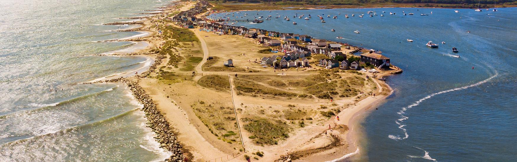 Aerial shot of mudeford beach on a sunny day with beach huts cascading into the distance
