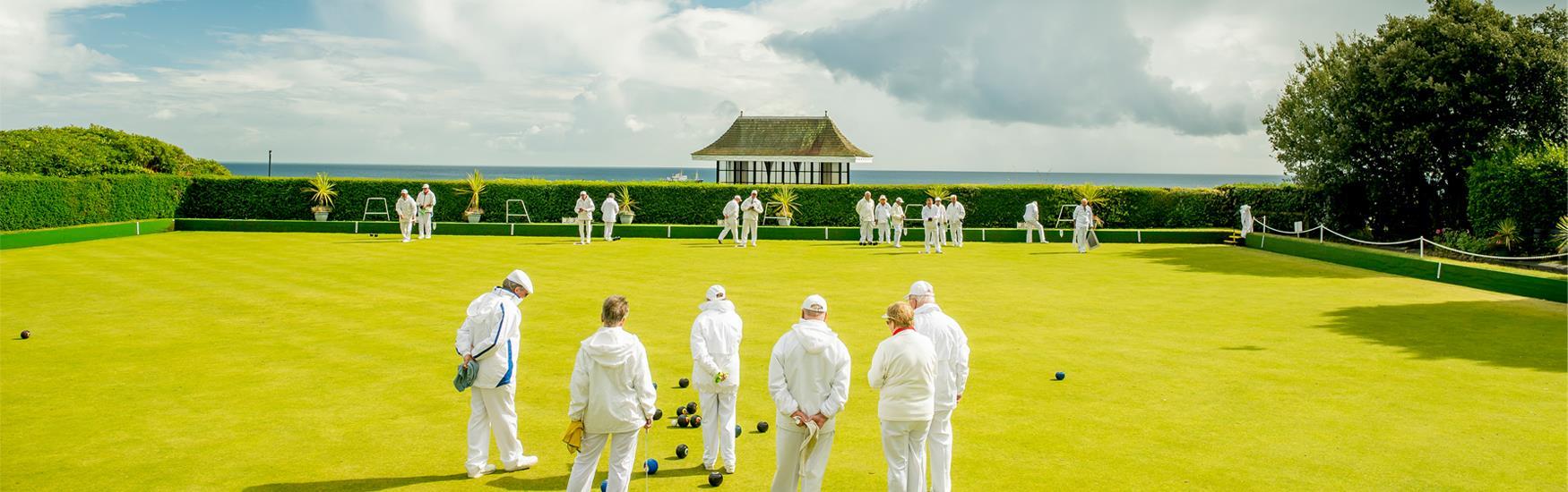 Group of people playing bowls on lush green grass with a stunning view of the sea