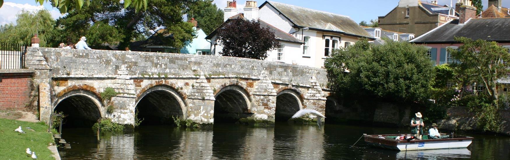 Christchurch stone bridge basking in the summer sun with two men fishing in a boat