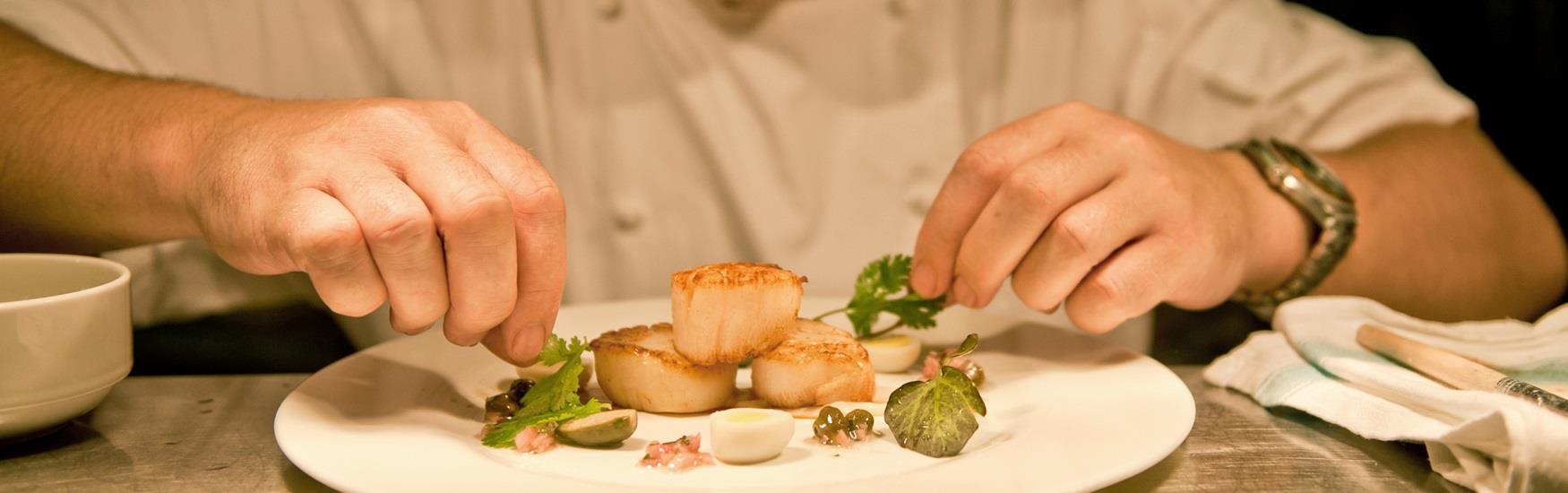 Chef's hands assembling scallops to serve