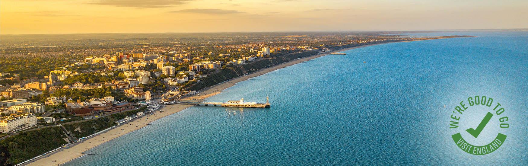 Sunset image of Bournemouth Bay beach and clifftops with green we're good to go logo in the corner