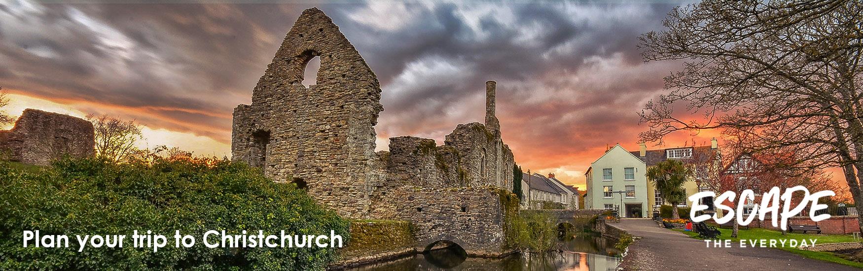 Red fiery sunset behind Christchurchs historic castle ruins with a logo overlay that reads "escape the everyday"