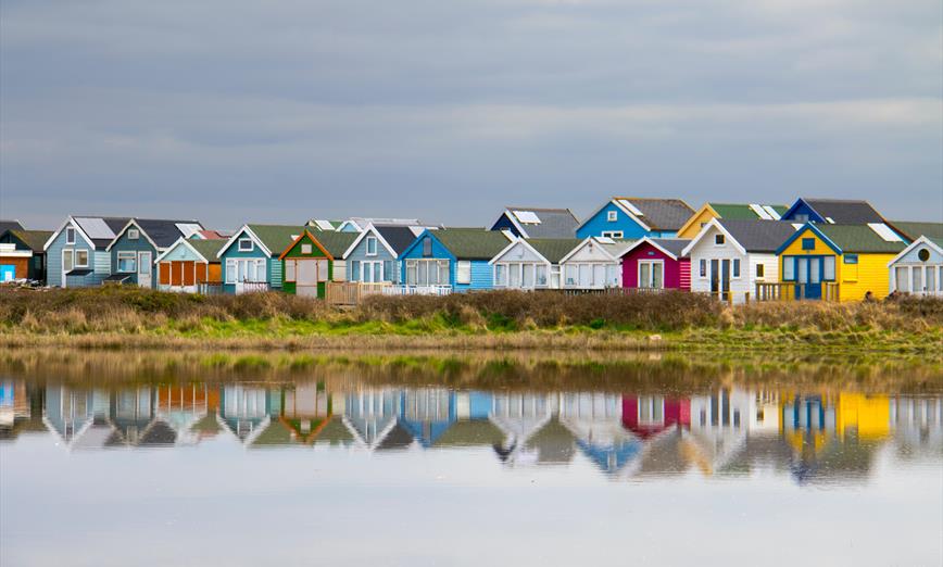 Multi coloured beach huts along mudeford beach and reflection on the calm sea 