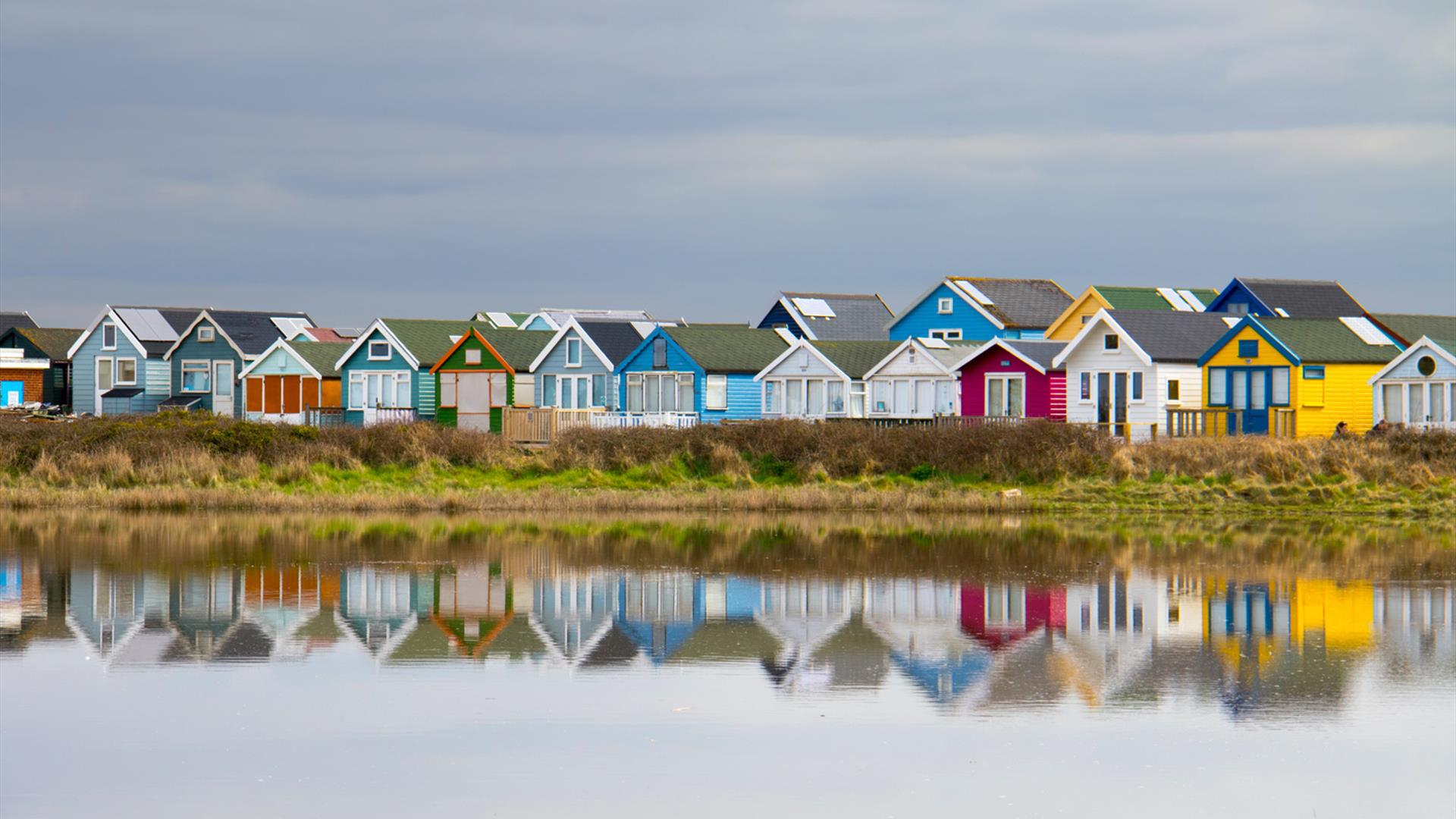 Multi coloured beach huts along mudeford beach and reflection on the calm sea