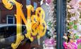 reflection of the shop window embossed with the letters N&B and some pink spring flowers to the side.
