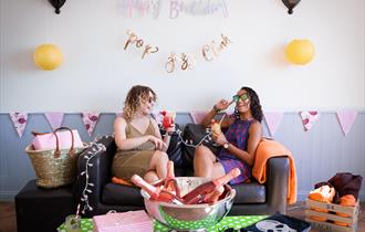 Two venue guests laughing and drinking on a sofa inside the decorated venue
