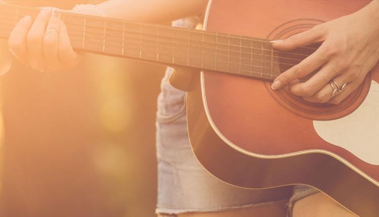 Close up of musician playing an acoustic guitar outdoors in the sunshine