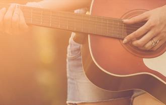 Close up of musician playing an acoustic guitar outdoors in the sunshine