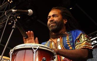 Caribbean man playing the conga drums in front of a microphone wearing traditional costume